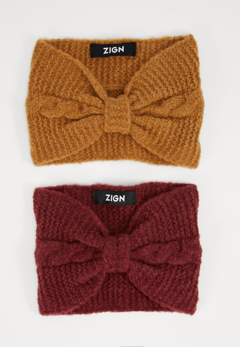 Two knitted headbands: one in mustard with a central bow, textured; one in burgundy with a similar design, both labeled "ZIGN."