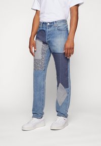 Blue denim jeans featuring various fabric patches in shades of blue, including floral and textured patterns, with a straight-leg cut.