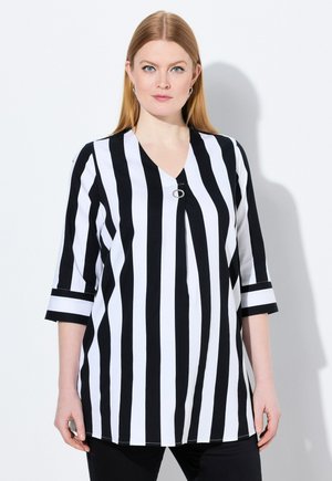 Blouse rayée noir et blanc avec un col en V, des manches trois-quarts et un détail argenté au niveau du col. Texture de tissu lisse.