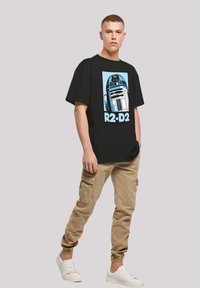 Svart T-skjorte med R2-D2-grafikk i blått og hvitt. Kombinert med khaki cargo-bukser og hvite joggesko. Enkel, uformell design.