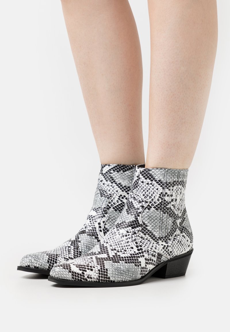 Botas de tornozelo com padrão de pele de cobra em preto e branco, apresentando um bico pontiagudo e um salto bloco baixo. Feitas de material sintético.