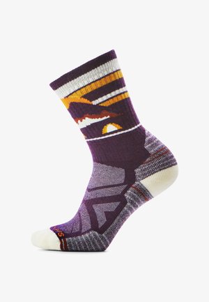 Fioletowa skarpetka z pomarańczowym, białym i żółtym wzorem przedstawiającym zachód słońca i góry, z amortyzowaną piętą i palcem oraz ściągaczem, na białym tle.