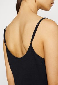 Camisola preta de alças finas, com decote redondo e textura suave, apresentando um close-up do design nas costas e na área dos ombros.