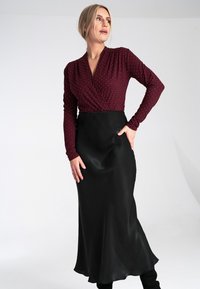 Czerwona bluzka z długim rękawem w stylu kopertowym w białe kropki zestawiona z czarną satynową spódnicą, charakteryzującą się gładką teksturą i sylwetką w kształcie litery A.