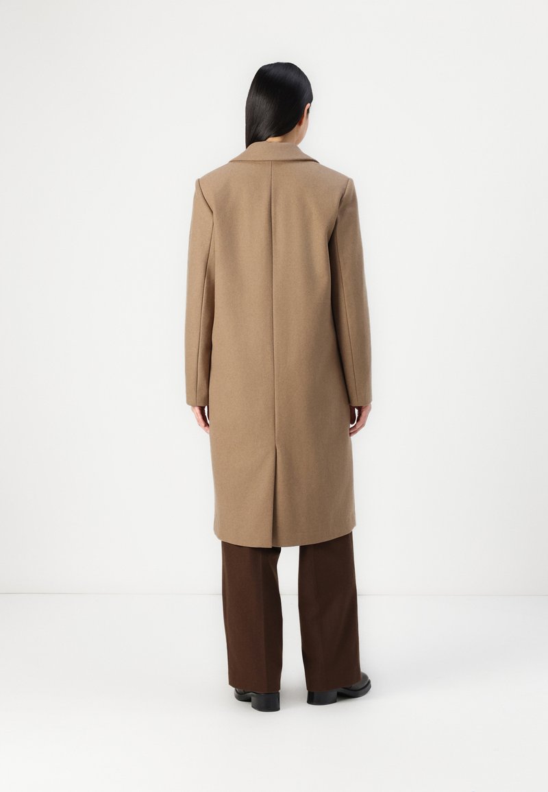 Cappotto lungo marrone con silhouette dritta, design monopetto e colletto a revers. Tessuto testurizzato con finitura liscia.