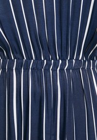 Gros plan sur un tissu bleu marine avec des rayures blanches verticales et un détail élastique froncé à la taille.