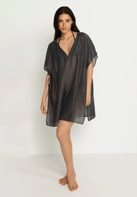 Prozirni crni plašt s V-izrezom, kratkim rukavima i bočnim prorezima za lakše kretanje, izrađen od lagane, lepršave tkanine.