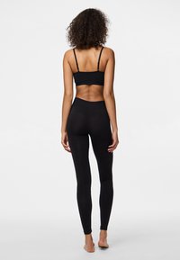 Svart sportig bralette med tunna remmar, matchad med högmidjade svarta leggings. Slät textur, figurnära design och inga synliga mönster.