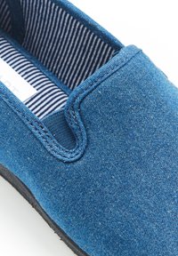 Blauwe spijkerbroek instapschoen met een textuur bovenkant. Interieur met blauw en wit gestreepte stof. Zwarte rubberen zool met zichtbare stiksels.