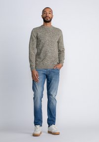Gehaakte ronde hals trui in een gestructureerde grijs-bruin mix, gecombineerd met lichtblauwe spijkerbroek en witte sneakers met rubberen zolen.
