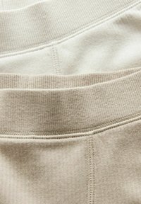 Drie paar geribbelde taillebanden in verschillende tinten beige en crème, met een beetje textuur en contrasterende stikdetails.