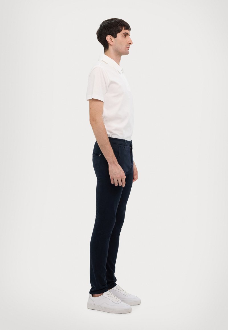 Hvit polo skjorte, mørkeblå slim-fit bukser og hvite sneakers. Profilvisning viser enkelt design og klassisk fargekombinasjon.