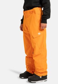 Heldere oranje snowboardbroek met een ontspannen pasvorm, gemaakt van duurzaam materiaal. Kenmerken zijn zijzakken en een logo-accent op het onderbeen.