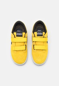 Pantofi de skateboard din suede galben cu accente negre, având două curele Velcro, un design perforat la vârf și o talpă din cauciuc alb.