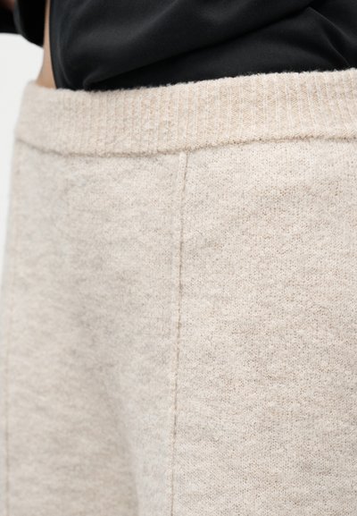 Μπεζ πλεκτό παντελόνι με ριμπ ελαστική ζώνη μέσης, φορεμένο με μαύρο τοπ, εστιασμένο στην περιοχή της μέσης και του άνω ισχίου.