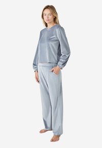 Conjunto de loungewear de terciopelo en azul claro; incluye una sudadera de corte relajado con mangas largas y pantalones con cintura elástica y bolsillos laterales.
