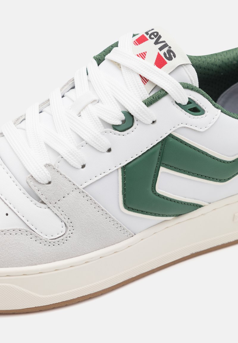 Weißer Sneaker mit grünen Akzenten, ausgestattet mit einem strukturierten Wildledereinsatz, glatten Lederseiten und einer Gummisohle. Schnürsenkel und Logo sichtbar.