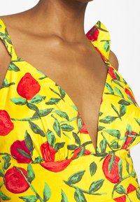 Vestido amarillo con un escote en V profundo, que presenta un vibrante estampado de rosas rojas y hojas verdes. Hecho de una tela suave con tirantes.