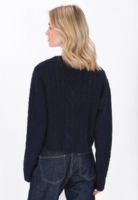 Pulover din lână tricotat cu model de sârmă de culoare bleumarin, cu design scurt, model texturat și tiv râbdat. Dispune de mâneci lungi și un croi confortabil.