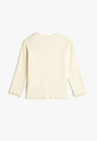 Haut à manches longues léger beige en tissu côtelé, avec un ourlet et des poignets à volants. Encolure ronde simple, texture douce et silhouette ajustée.