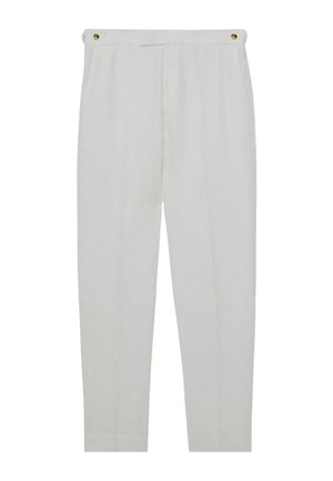 Osoba o ciemnej karnacji ubrana w biały garnitur z guzikami, ręka w kieszeni, ukazująca fakturę tkaniny oraz dopasowanie rękawa i spodni.