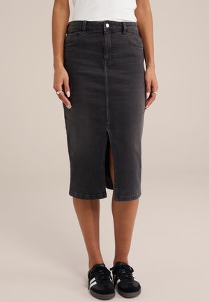 Vrouw draagt een zwarte denim midi-rok met een split aan de voorkant, een wit top, zwart-witte sneakers en zilveren ringen aan haar vingers.