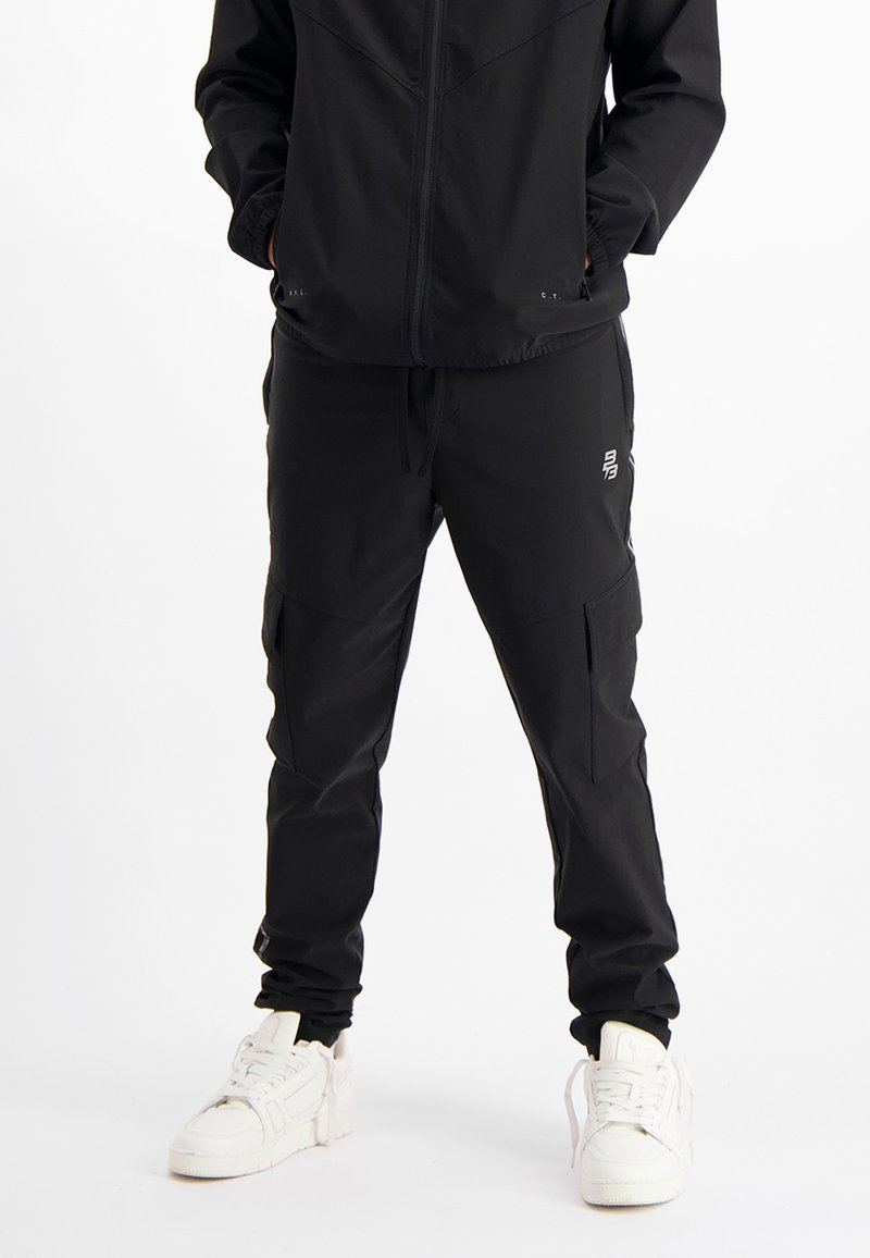 Zwarte sportbroek gemaakt van lichtgewicht materiaal, met een relaxte pasvorm, zijzakken en subtiele branding op de dij.