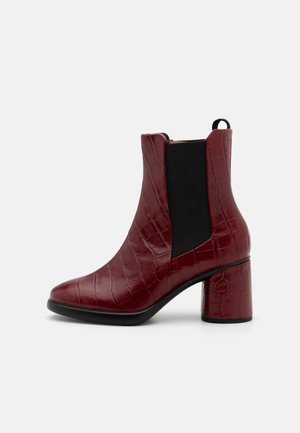 Bottine bordeaux à texture crocodile, talon carré, panneau latéral élastique noir et languette de tirage sur fond gris.