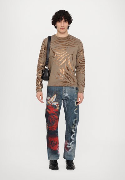 Beige sweater with metallic zebra stripes, paired with blue denim pants featuring a red rose design and white text. Black crossbody bag.