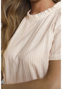 Ljusrosa blus med subtila vertikala ränder, volangkrage, korta ärmar, mjuk textur och andningsbart tyg.