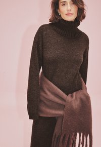 Tmavohnedý rolák vyrobený z mäkkého materiálu, doplnený svetlohnedým šálom s třásňami stylizovaným okolo pása.