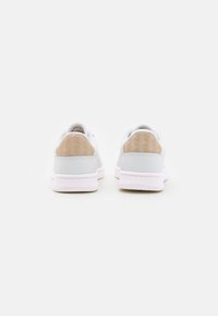Des baskets blanches avec un dessus lisse, des accents gris clair et des languettes de talon à motif beige. Elles possèdent une semelle extérieure rose et un design minimaliste.
