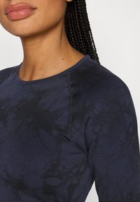 Μπλούζα με μακριά μανίκια σε σκούρο ναυτικό μπλε χρώμα με διακριτικό μοτίβο tie-dye, κατασκευασμένη από απαλό ύφασμα. Διαθέτει στρογγυλή λαιμόκοψη και εμφανείς ραφές.