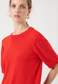 Rød strikket kortermet t-skjorte med rund hals. Stoffet har en glatt tekstur med et rent, minimalistisk design uten synlige mønstre.