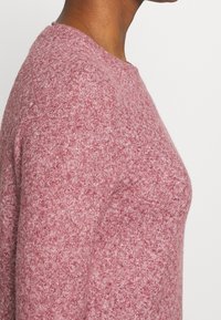 Pullover lavorato a maglia in un morbido tessuto rosa con texture, dotato di un collo rotondo. Presenta una silhouette aderente e polsini a costine.