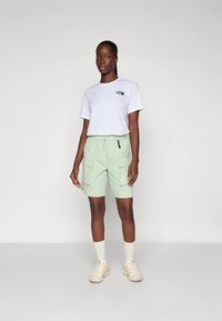 Valge t-särk väikese graafikaga, kombineeritud heleroheliste lahtiste pükstega, millel on küljetaskud ja elastne vöökoht. Kreemjad tossud.