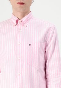 Person wearing a pink and white vertically striped button-up shirt with a chest pocket and a small embroidered logo.