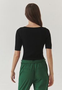 Haut noir à rayures et manches courtes avec un décolleté large, associé à un pantalon taille haute vert avec poches latérales et une texture douce.