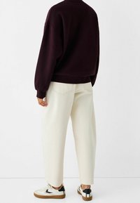 Felpa oversize bordeaux, pantaloni ampi color crema e sneakers bianco e nero. I dettagli notevoli includono polsini elasticizzati e tasche posteriori.