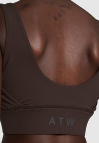 Brun sport-bh med en scoop-back-design, breda axelremmar, texturerat tyg och en "ATW"-logotyp i grått längs bandet.