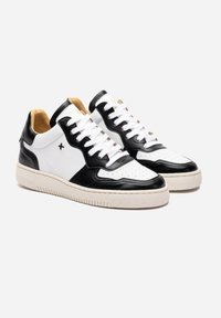 Sneakers in pelle bianco e nero con dettagli perforati, lacci piatti e suola in gomma beige. Presentano cuciture a contrasto e un design minimalista.