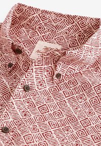 Chemise à manches courtes présentant un motif géométrique rouge sur un fond clair, avec un col et des boutons marron, fabriquée en tissu texturé.