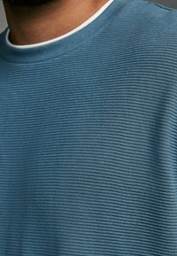 Sweat-shirt bleu à côtes avec un tissu texturé. Col rond avec un col intérieur blanc subtil. Matière douce et légère.