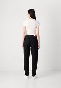 Mustat suorat farkut korkealla vyötäröllä, joissa on brändilogo takana. Yhdistetty tiukkaan valkoiseen t-paitaan ja valkoisiin lenkkareihin.