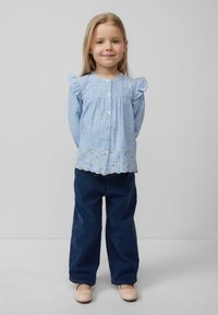 Hellblau und weiße gestreifte Bluse mit Rüschensch sleeves und floralem Stickerei am Saum, kombiniert mit dunkelblauen Hosen und hellen Schuhen.