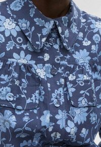 Navy blue floral shirt featuring light blue flowers, pointed collar, two chest pockets, and button front closure with matching buttons.