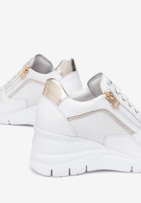 White sneakers with a smooth leather and mesh upper, gold hardware accents, and a wedge sole. Features side zipper and padded collar.