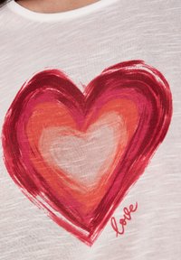 T-shirt blanc avec un grand design de cœur rouge multicolore au toucher brossé ; le mot "amour" est imprimé en rouge près du cœur.