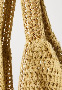 Sac en crochet jaune avec un design texturé et à mailles ouvertes. Équipé de détails métalliques dorés sur les poignées pour une touche supplémentaire.