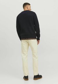 Maglione a coste blu navy con scollatura rotonda, pantaloni crema e scarpe nere. Tessuto delicato sul maglione e sui pantaloni. Design semplice e classico.